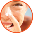 Smiling woman applying sunscreen lotion onto nose.